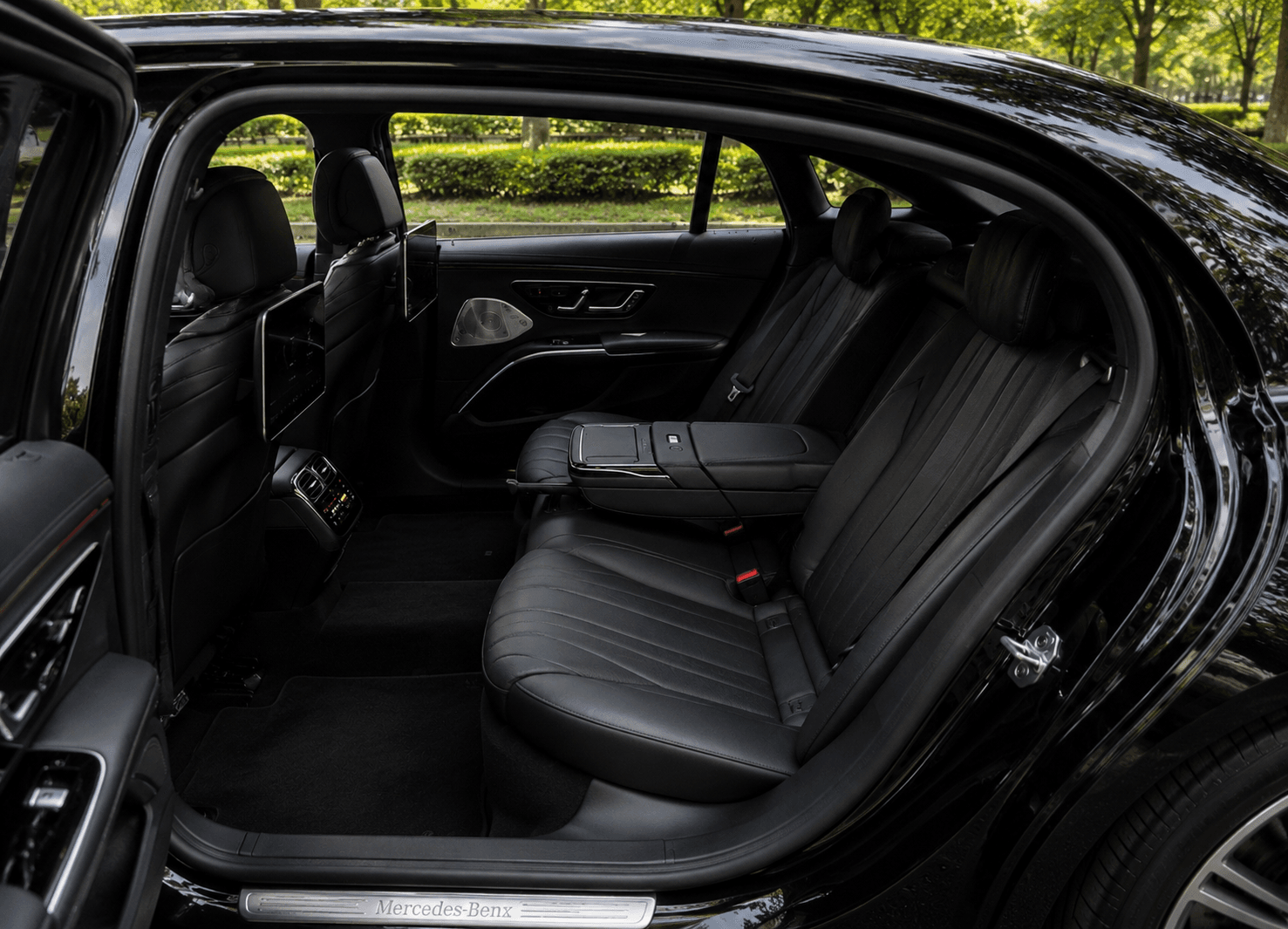 Luxurious black leather rear seats of a Mercedes-Benz featuring entertainment screens and an open door.