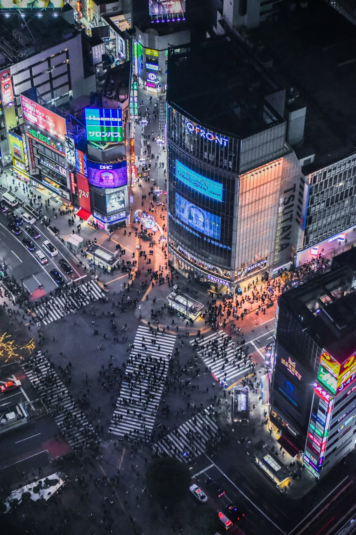 Aerial view of Tokyo's Shibuya Crossing at night with crowds and bright neon billboards.