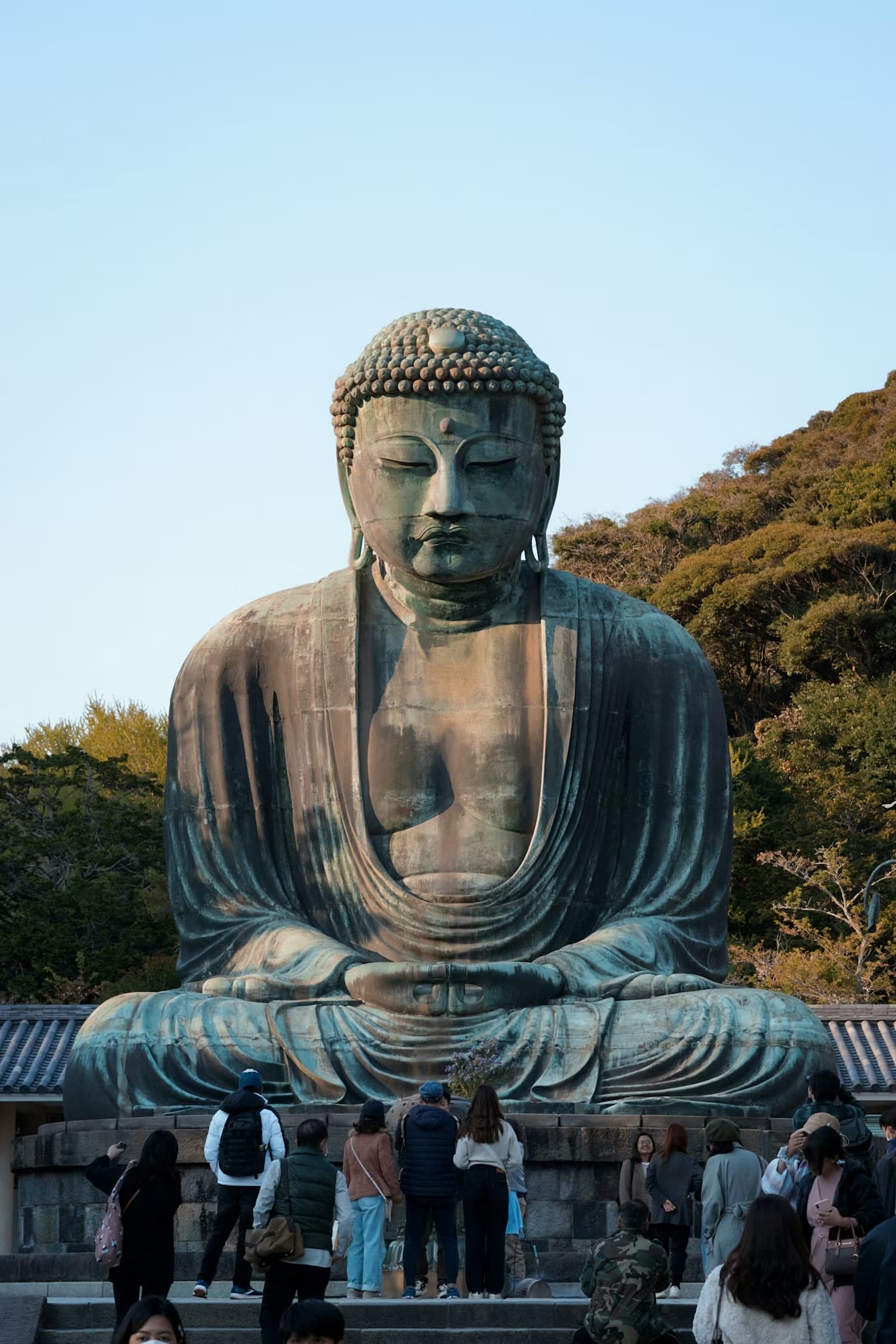 Massive bronze Great Buddha of Kamakura statue sitting in meditation with tourists at its base.